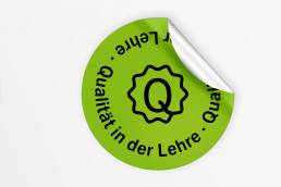 Mockup für einen Logo-Sticker von Qualität Lehre. Das neue Logo von Qualität Lehre wurde von i-kiu gestaltet.